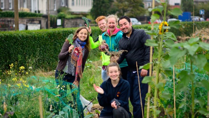 A group of community gardeners showing the vegetables they have grown including courgettes and beetroots and surrounded by their urban garden.
