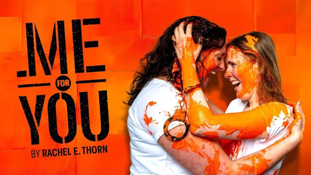 Two women with huge grins on their faces embrace, staring deep into each other's eyes. They're covered in orange paint and one of them has handcuffs dangling from her wrist. Text in a graffiti stencil font reads Me For You by Rachel E. Thorn